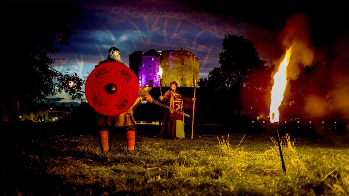 A Viking with a shield, a flaming torch and a woman standing in front of Clifford’s tower at night